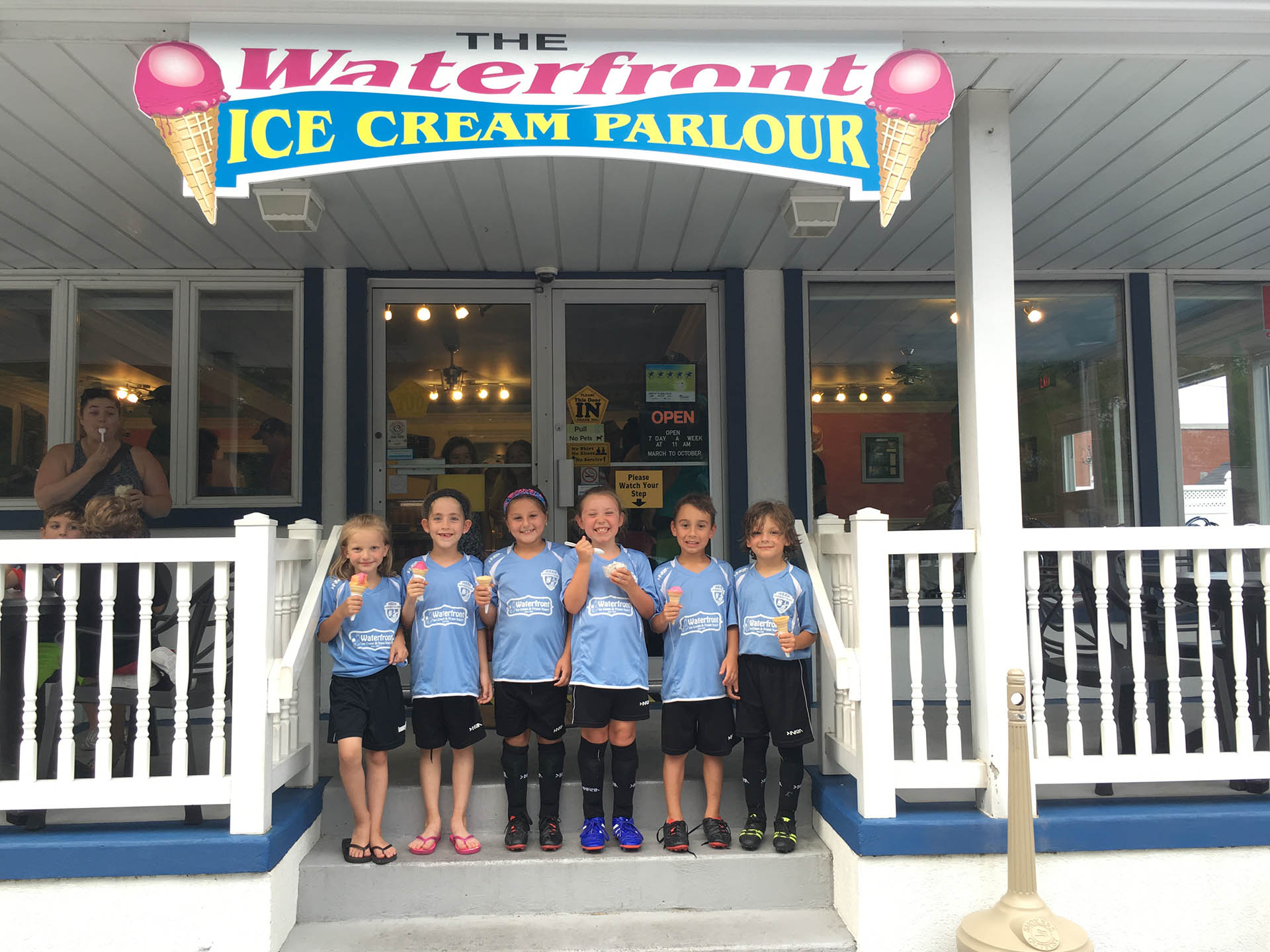 A group of kids standing in front of the entrance to an ice cream parlor.