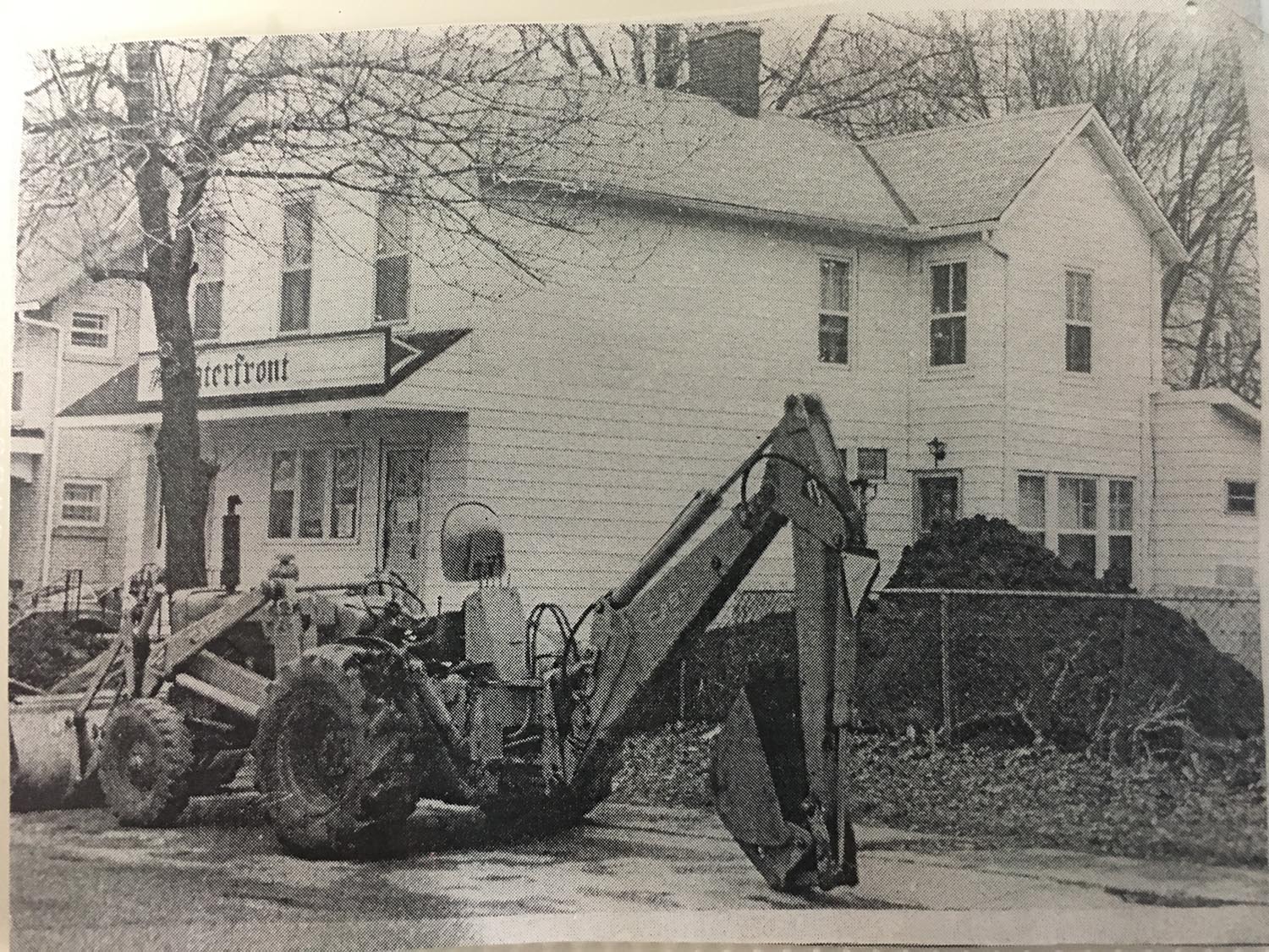 A black and white photo of a tractor in front of a house.